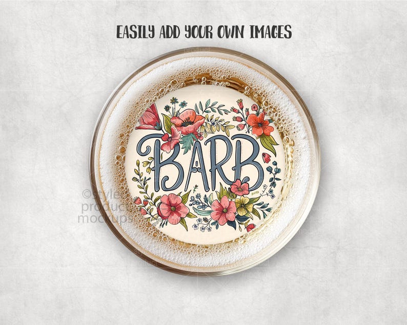 May include: A round coaster with the name "BARB" in blue script, surrounded by a floral wreath of red, pink, and yellow flowers with green leaves. The coaster is inside a clear glass with a bubbly liquid.