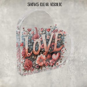 Pu&ograve; includere: Decorazione trasparente a forma di cuore con la parola "LOVE" in lettere color corallo. Le lettere sono circondate da un motivo floreale ad acquerello nei toni del rosa, del rosso e del blu. Il testo "SHOWS CLEAR ACRYLIC" &egrave; in alto.