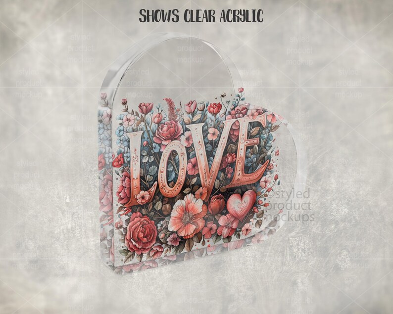 Pu&ograve; includere: Decorazione trasparente a forma di cuore con la parola "LOVE" in lettere color corallo. Le lettere sono circondate da un motivo floreale ad acquerello nei toni del rosa, del rosso e del blu. Il testo "SHOWS CLEAR ACRYLIC" &egrave; in alto.