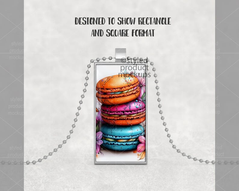 May include: A silver chain necklace with a rectangular pendant featuring a stack of colorful macarons. The macarons are decorated with white frosting and flowers.
