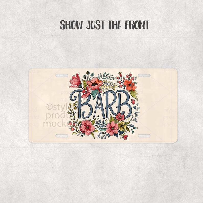 May include: A beige license plate featuring the name "BARB" in a blue, cursive font, encircled by a floral wreath of pink, red, and yellow flowers and green leaves. The text "SHOW JUST THE FRONT" is at the top.