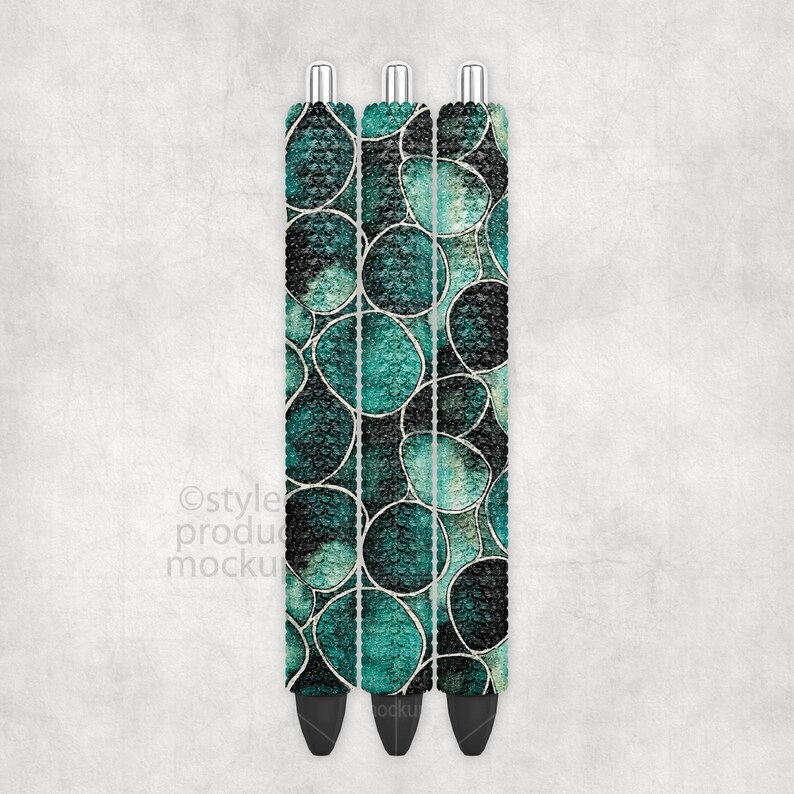 May include: Three pens with a teal and black abstract pattern. The pens have silver tips and black ink tips. The pattern is made of circles and lines. The pens are on a white background.
