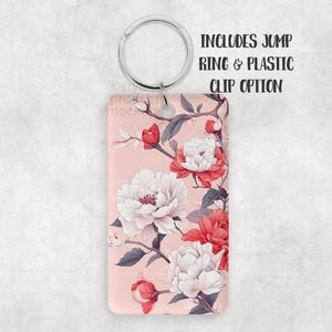 K&ouml;nnte beinhalten: Rechteckiger Schl&uuml;sselanh&auml;nger mit floralem Design. Der Schl&uuml;sselanh&auml;nger hat einen rosa Hintergrund mit wei&szlig;en und roten Pfingstrosen und grauen Bl&auml;ttern. Der Text "INCLUDES JUMP RING & PLASTIC CLIP OPTION" ist oben rechts aufgedruckt.