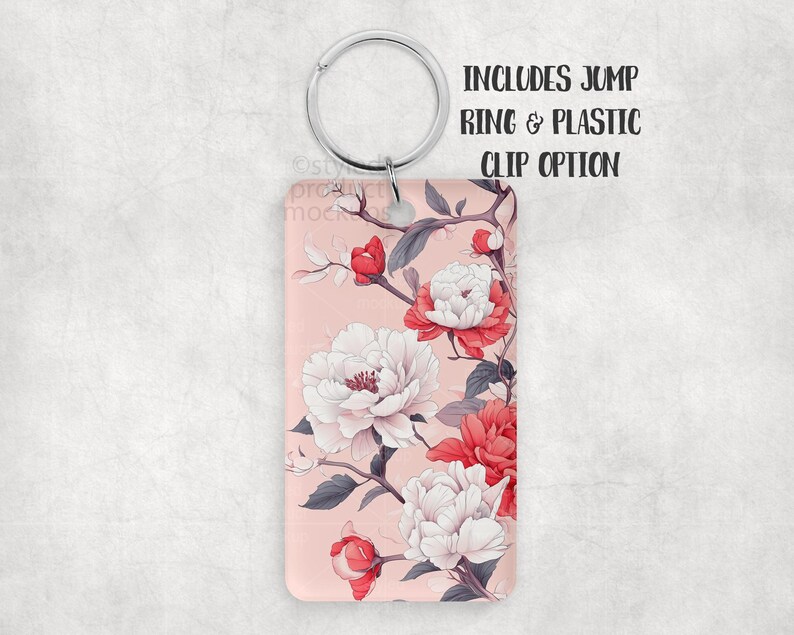 K&ouml;nnte beinhalten: Rechteckiger Schl&uuml;sselanh&auml;nger mit floralem Design. Der Schl&uuml;sselanh&auml;nger hat einen rosa Hintergrund mit wei&szlig;en und roten Pfingstrosen und grauen Bl&auml;ttern. Der Text "INCLUDES JUMP RING & PLASTIC CLIP OPTION" ist oben rechts aufgedruckt.
