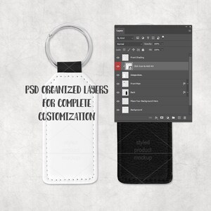 以下が含まれることがあります： シルバーのリングと黒いストラップが付いた白い革のキーホルダーモックアップ。キーホルダーには「PSD ORGANIZED LAYERS FOR COMPLETE CUSTOMIZATION」の文字がプリントされています。キーホルダーの下には黒い革の長方形があります。右側にはPhotoshopのレイヤーパネルがあります。