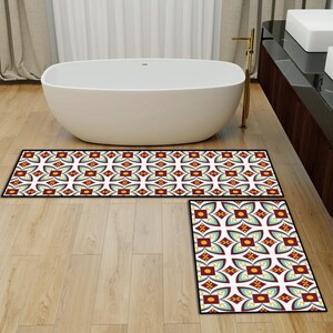 May include: Two-piece bathroom rug set with a geometric floral pattern in burgundy, teal, yellow, and white. The rugs have a black border and are placed on a light wood floor near a white bathtub.