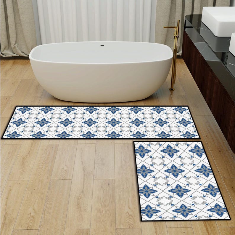 May include: Two-piece bathroom rug set featuring a white background with a repeating blue floral pattern. The rugs have a black border and are placed on a light wood floor near a white bathtub.
