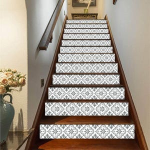 May include: A wooden staircase with decorative gray and white patterned stair risers. The risers feature a floral design. The stairs have a dark brown wooden handrail and trim. A vase of flowers is visible on the left side of the image.