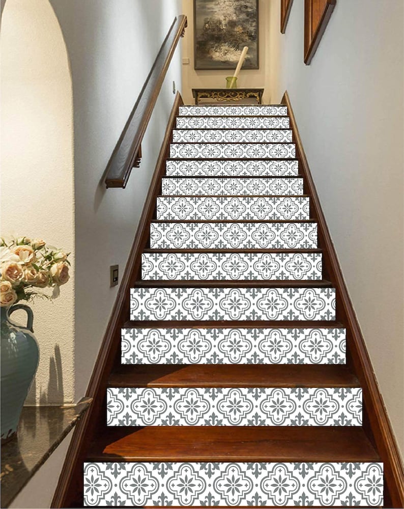 May include: A wooden staircase with decorative gray and white patterned stair risers. The risers feature a floral design. The stairs have a dark brown wooden handrail and trim. A vase of flowers is visible on the left side of the image.