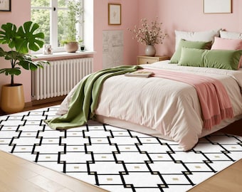 May include: A rectangular area rug featuring a white background with a repeating black geometric grid pattern and small gold square accents. The rug is positioned on a light wood floor in a bedroom with pink walls, a bed with green and pink bedding.