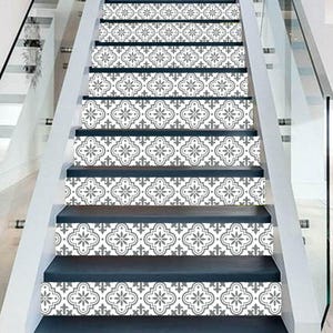 May include: Staircase with decorative tile stickers. The stickers feature a repeating gray and white floral pattern. The risers are a dark blue-gray color, and the stairs have a white trim and glass railing.