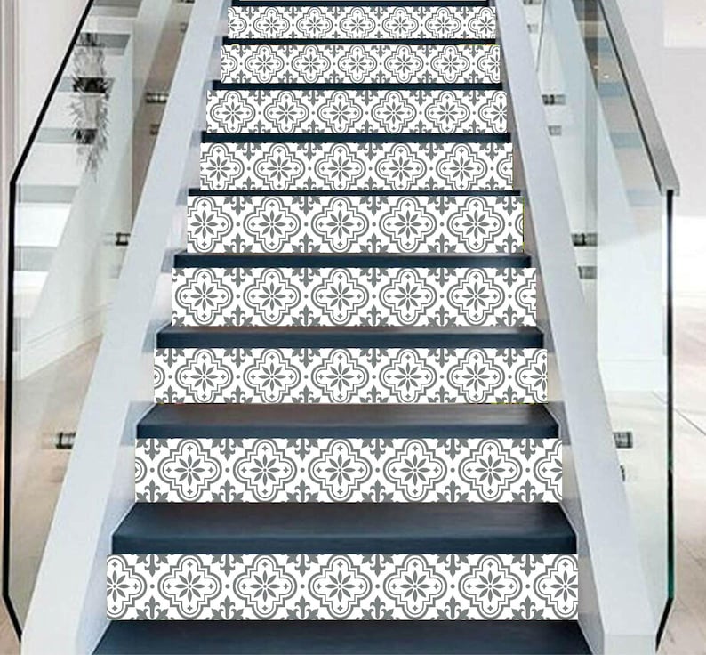 May include: Staircase with decorative tile stickers. The stickers feature a repeating gray and white floral pattern. The risers are a dark blue-gray color, and the stairs have a white trim and glass railing.