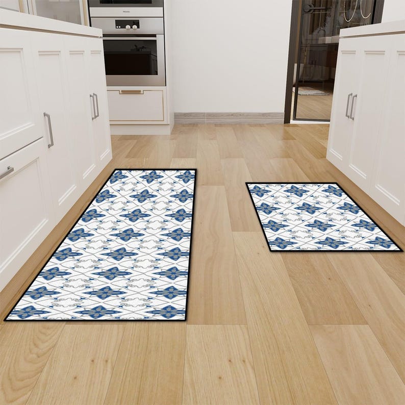 May include: Two rectangular kitchen mats with a blue and white floral pattern and black borders are displayed on a hardwood floor. The mats are in a kitchen setting, with white cabinets and appliances visible in the background.