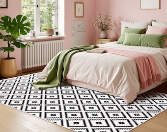 May include: A rectangular area rug featuring a repeating black and white geometric diamond pattern with jagged edges. The rug is positioned on a light wood floor in a bedroom setting, partially covered by a bed with pink, green, and white bedding.