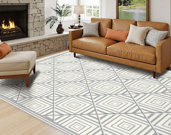 May include: A large area rug featuring a repeating geometric pattern of white and gray concentric diamonds and intersecting lines. The rug covers the floor in front of a brown leather sofa with decorative pillows and a stone fireplace.
