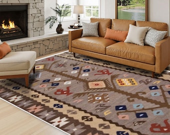 May include: A large rectangular area rug featuring a taupe background with a repeating geometric pattern in shades of brown, cream, blue, red, and yellow. The design includes stylized floral and diamond motifs arranged in horizontal bands.