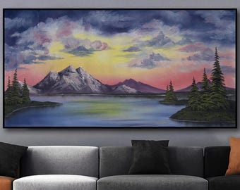 May include: Oil painting of a mountain landscape with a lake. The artwork features a sunset with a yellow and pink sky, dark clouds, and mountains. Green trees are on the lake's edge. The painting is framed in a black frame.