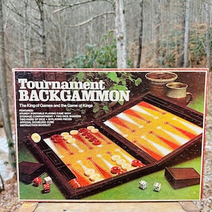 Puede incluir: Un juego de backgammon "Tournament" vintage. La caja presenta el nombre del juego y un gráfico del tablero de juego abierto con acentos rojos, blancos y amarillos. Incluye dados, fichas y un cubo de duplicación. El juego está en un estuche marrón.
