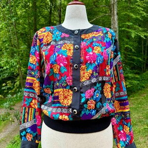 Può includere: Giacca vintage con stampa floreale con colletto, finiture e polsini neri. La giacca presenta un vivace motivo di fiori rossi, gialli, blu e viola. Ha un orlo a coste nero ed è abbottonata sul davanti.