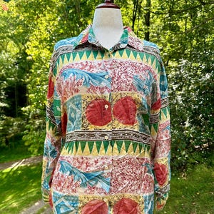 May include: A long-sleeved button-down shirt with a colorful, patterned design. The shirt features a collared neckline and a vibrant mix of red, green, yellow, and blue geometric and floral patterns. The shirt is displayed on a mannequin.