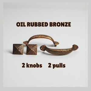 May include: Oil rubbed bronze cabinet hardware set. The set includes two square knobs and two pulls. The hardware has a hammered texture and a dark brown finish. The text "2 knobs 2 pulls" is below the hardware.