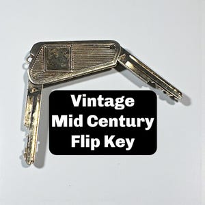 May include: A vintage silver-toned flip key with a rectangular body and two folding key blades. The key has a textured design and the text "Vintage Mid Century Flip Key" is displayed on a black background.