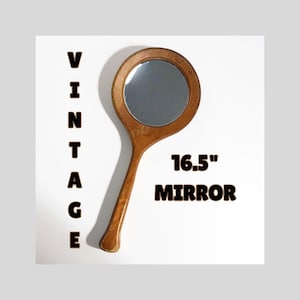 May include: Vintage hand mirror with a wooden handle and frame. The round mirror is 16.5 inches in length. The word "VINTAGE" is printed vertically on the left side of the mirror.