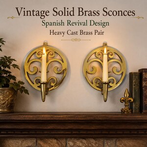 May include: A pair of circular solid brass wall sconces featuring an intricate openwork scroll design. Each sconce holds a single taper candle in a central brass cup. The text reads: Vintage Solid Brass Sconces, Spanish Revival Design, Heavy Cast Brass Pair.