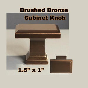 May include: Brushed bronze cabinet knob with a rectangular design. The knob measures 1.5" x 1" and features a square top and a sturdy base. The text "Brushed Bronze Cabinet Knob" is displayed at the top.