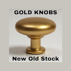 Pode incluir: Um puxador de armário dourado com um topo arredondado e uma base cilíndrica. O puxador tem a inscrição "GOLD KNOBS" e "New Old Stock" em texto preto. O hardware tem um acabamento metálico e é provavelmente para móveis.