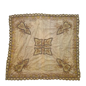 May include: A beige square tablecloth with a delicate floral pattern embroidered in gold and brown thread. The tablecloth has a scalloped edge and is adorned with small, sparkling beads.