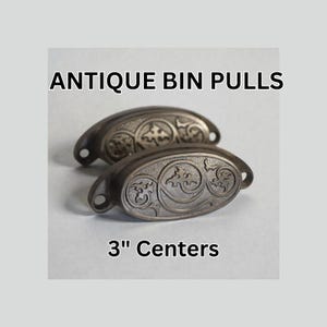 May include: Two antique bin pulls with ornate scrollwork and a dark, aged finish. The pulls are 3 inches apart, with a curved design and mounting holes. The text "ANTIQUE BIN PULLS" and "3" Centers" are displayed.