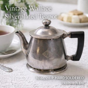 Puede incluir: Tetera plateada vintage de Wallace con asa negra. La tetera tiene un acabado plateado y un emblema en forma de diamante. El texto en la imagen dice "10 oz, 28-P HARD SOLDERED 1930s-40s Era".