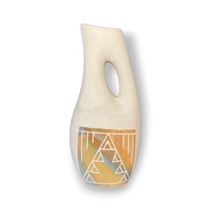 May include: A white ceramic vase with a geometric design in orange, yellow, and blue. The vase has a unique, curved shape with a cut-out handle.