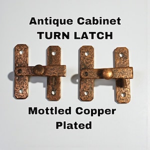 May include: Two mottled copper-plated antique cabinet turn latches. Each latch has an H-shaped design with a central rotating knob. The metal has a textured, aged appearance, with visible screw holes for mounting. The text "Antique Cabinet TURN LATCH" and "Mottled Copper Plated" is displayed.