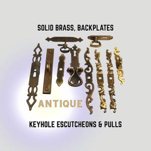 May include: A collection of antique solid brass backplates, keyhole escutcheons, and pulls. The hardware pieces feature intricate designs and a warm, aged patina. The word "ANTIQUE" is displayed in the image. Measurements are in centimetres.