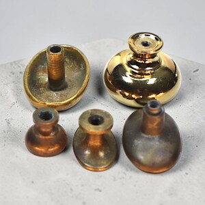 May include: A collection of antique brass cabinet knobs in different designs. The knobs include a large oval knob, a shiny gold round knob, and several smaller, rounded knobs. The brass has a warm, aged patina.