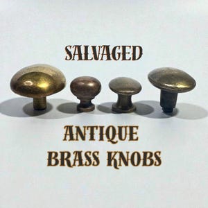 May include: Four antique brass knobs in varying sizes and shapes are displayed against a white background. The knobs have a tarnished, aged appearance. The text "SALVAGED" and "ANTIQUE BRASS KNOBS" are printed above and below the knobs.
