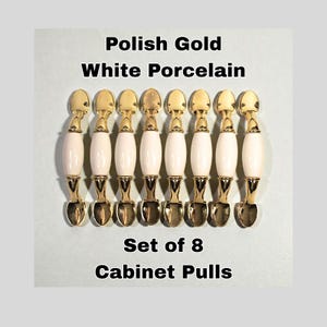May include: Set of eight cabinet pulls with a gold finish and white porcelain handles. The pulls have a spoon-like design and are arranged in a row. The text "Polish Gold White Porcelain" and "Set of 8 Cabinet Pulls" is displayed.