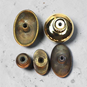 May include: A selection of antique brass cabinet knobs and pulls. The knobs are in various shapes, including oval and round. Finishes vary from polished gold to aged brass, showing different textures and patinas. These hardware pieces are suitable for furniture restoration projects.