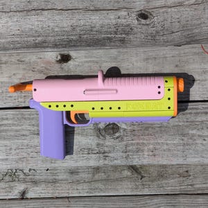 May include: A pink, yellow, and purple toy gun with the word "FOXBAT" printed on the side.