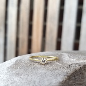 Op de afbeelding: Een delicate gouden ring met een enkele, ronde, heldere edelsteen in een kraalbezetting.