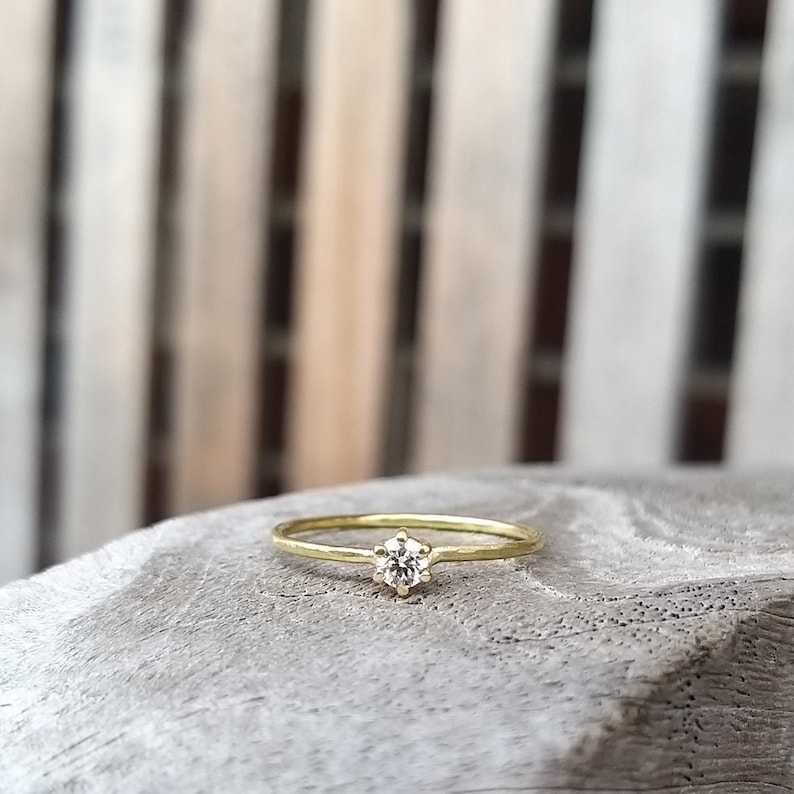 Op de afbeelding: Een delicate gouden ring met een enkele, ronde, heldere edelsteen in een kraalbezetting.