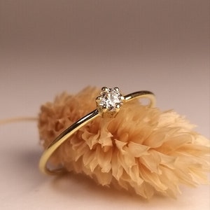 Op de afbeelding: Een delicate gouden ring met een enkele, kleine, ronde diamant in een kraalbezetting.