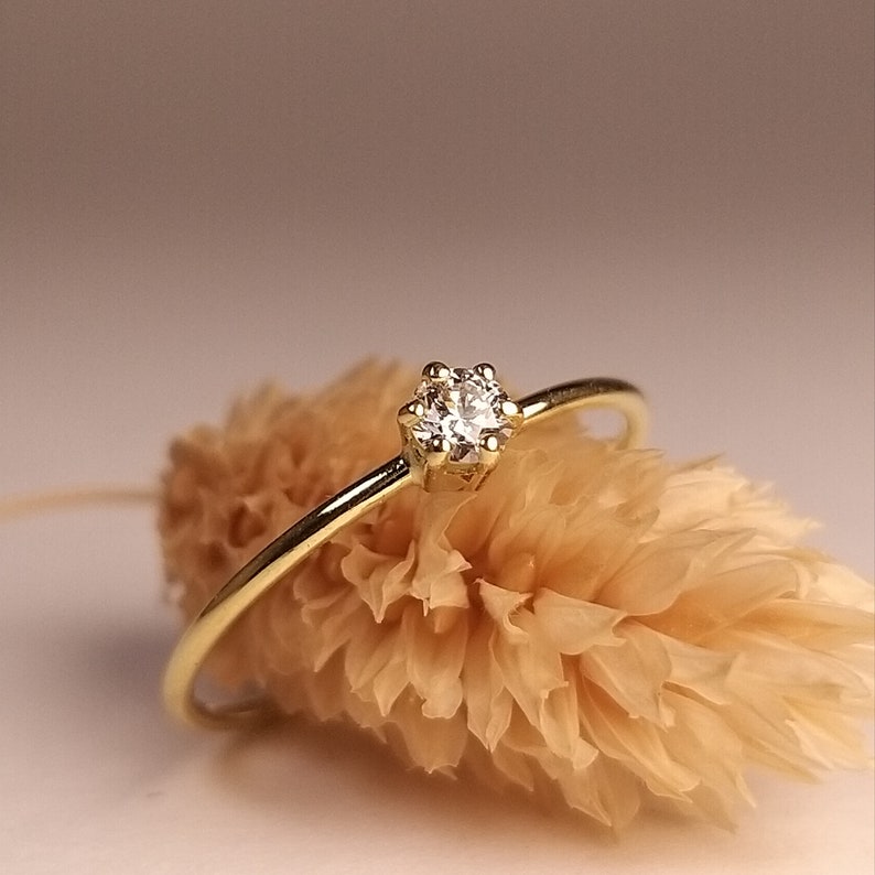 Op de afbeelding: Een delicate gouden ring met een enkele, kleine, ronde diamant in een kraalbezetting.