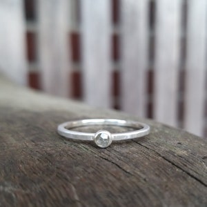 Könnte beinhalten: Ein silberner Ring mit einem kleinen, runden, klaren Diamanten in der Mitte.