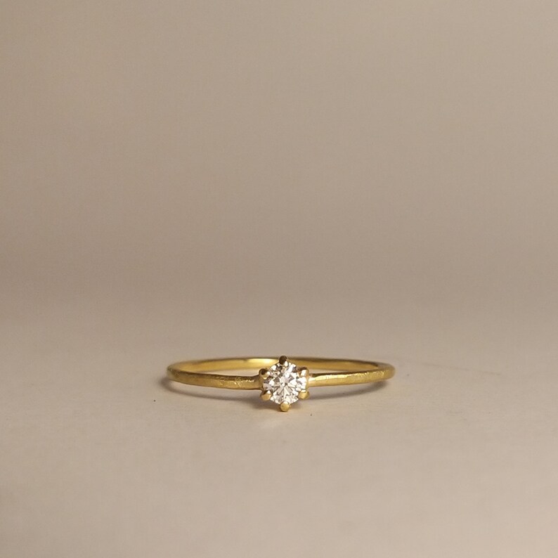 Op de afbeelding: Een delicate gouden ring met een enkele, ronde, heldere diamant in het midden.