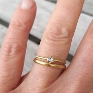 Op de afbeelding: Twee gouden trouwringen aan een vinger. De bovenste ring heeft een kleine, ronde, heldere diamant.