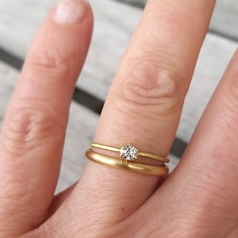 Op de afbeelding: Twee gouden trouwringen aan een vinger. De bovenste ring heeft een kleine, ronde, heldere diamant.
