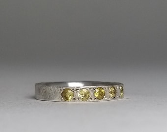 Op de afbeelding: Een zilveren ring met een rij kleine, ronde, gele edelstenen.